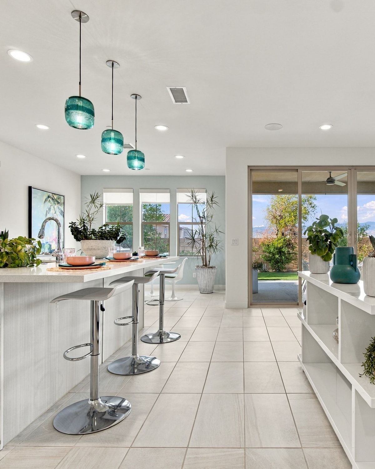Bright open kitchen with teal pendant lights, island bar stools and patio doors