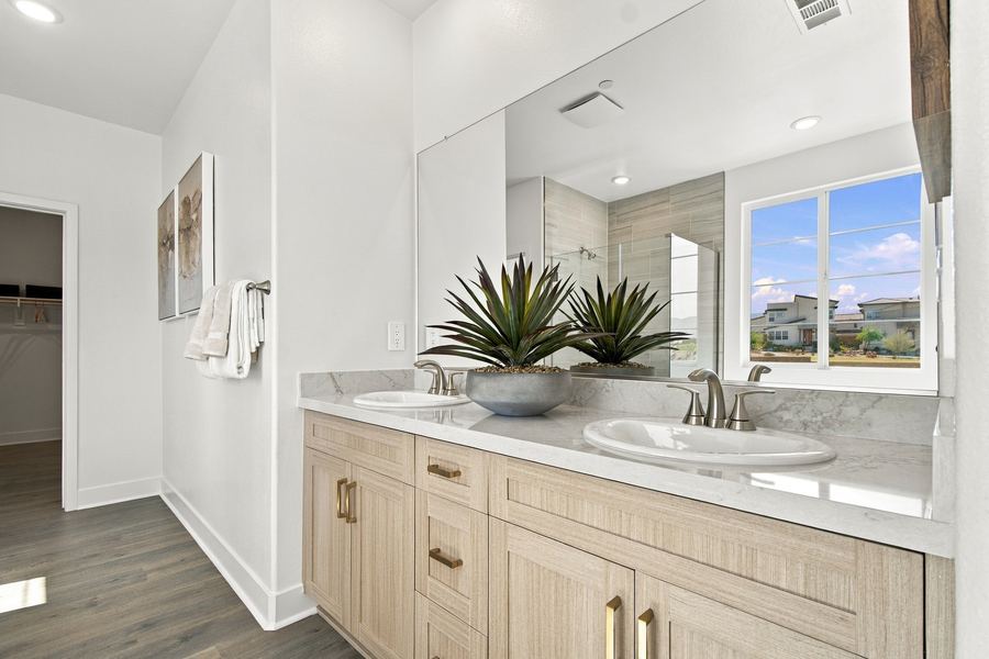 Primary bathroom double vanity with light wood cabinetry